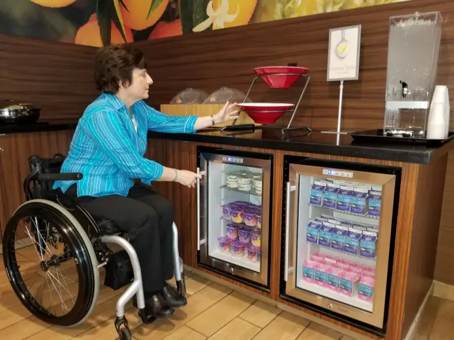 Rosemarie Rossetti straining to reach a serving container with ladle of maple syrup on a buffet line.